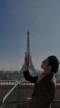 a woman is standing in front of the eiffel tower with her hand up