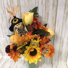 a vase filled with yellow and orange flowers on top of a wooden table next to a white wall