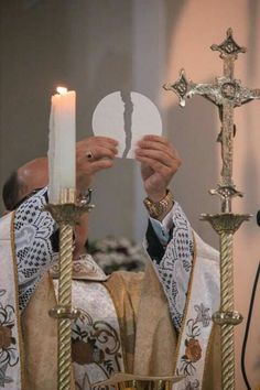 the priest is holding up a piece of paper in front of his face as he holds a lit candle