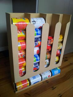 an open cardboard box filled with cans and cans on top of a wooden floor next to a wall