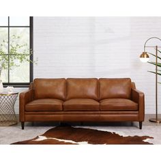 a brown leather couch sitting in front of a large window next to a cowhide rug