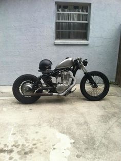 a black motorcycle parked in front of a blue building with a window on the side