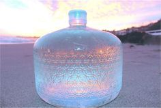 a large blue bottle sitting on top of a sandy beach next to the ocean at sunset