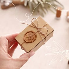 a hand holding a small wooden box with a wax stamp on it and string tied around the top