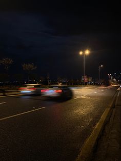 a car driving down the road at night with street lights and buildings in the background