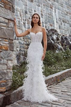 a woman in a white wedding dress standing next to a brick wall with her hand on her hip