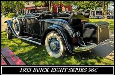 an old black car parked on the grass in front of a building with a sign that says, 1933 buick eight series 66c