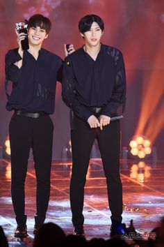 two young men standing next to each other on a stage holding cell phones in their hands