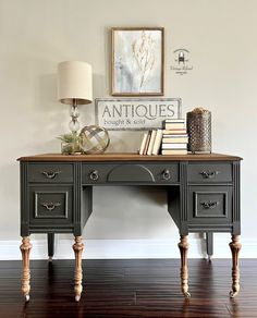 an antique desk with books, lamp and pictures on the wall