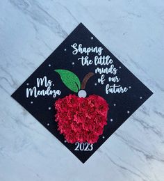 a graduation cap decorated with red roses on top of a white marble surface and the words, shaping the little minds of our future