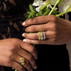 two hands with wedding rings on their fingers holding a bouquet of white and yellow flowers