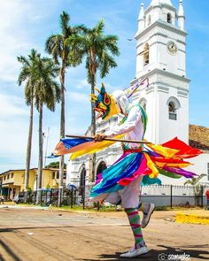 a man dressed in colorful clothing and holding a large multicolored kite next to a tall white building