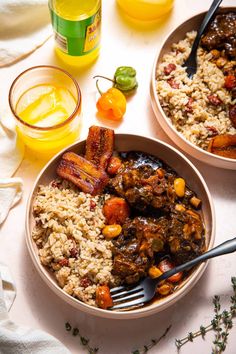 two bowls filled with rice, meat and vegetables next to orange juice on a table