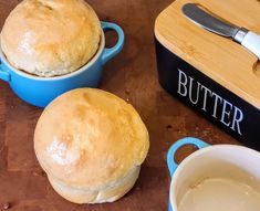 two round bread rolls sitting on top of a wooden table next to a butter container