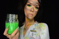 a woman is holding a jar with green paint on her face and she has black hair