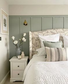 a white bed sitting in a bedroom next to a nightstand with flowers on top of it