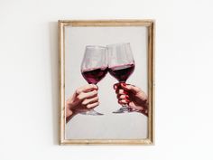 two hands holding wine glasses in front of a white wall with a painting on it