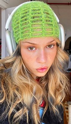 a woman with headphones on her ears wearing a green knitted hat and looking at the camera