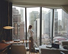 a woman standing in front of a window looking out at the cityscape and skyscrapers