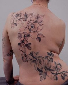 the back of a woman's body with flowers tattooed on her upper and lower half