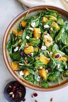 a salad with spinach, cranberries and nuts in a bowl on a table