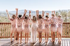 a group of women in pink robes standing on a wooden deck with their arms up