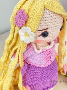 a crocheted doll with blonde hair wearing a purple dress and flower in her hair