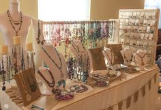 a table topped with lots of necklaces and bracelets on display next to a window