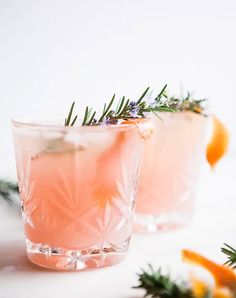 two glasses filled with pink lemonade and rosemary garnish on a white surface