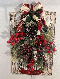 a christmas wreath hanging on the wall with pine cones, berries and evergreens attached to it