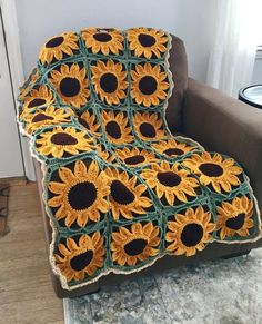 a crocheted blanket with sunflowers on it sitting in a chair next to a window