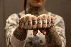 a man with tattoos on his arms holding up the word overcome in front of him