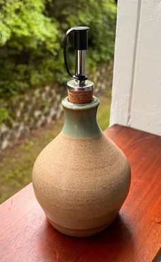 a brown and green vase sitting on top of a wooden table next to a window