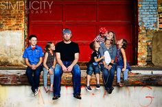 a group of people sitting next to each other on top of a wooden bench in front of a red door