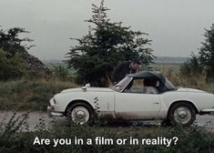 an old car sitting in the middle of a field with trees and bushes around it