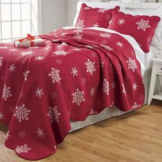 a red bed with white snowflakes on it and a christmas present under the covers