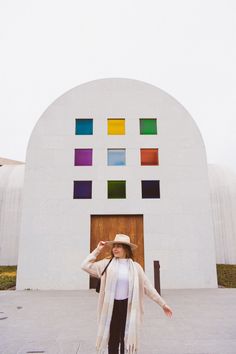 a woman standing in front of a white building with multicolored squares on it