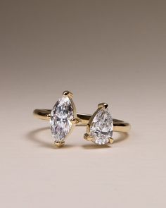 two pear shaped diamond engagement rings on a plain surface, set in yellow gold and white gold