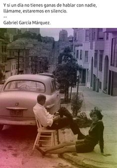 two men sitting on a bench in front of a car and another man standing next to them