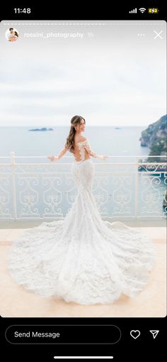 a woman in a white wedding dress standing on a balcony looking at the ocean with her arms outstretched