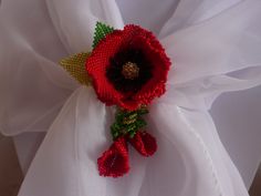 a red flower with green leaves and beads on it's center is sitting on a white cloth