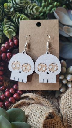 two white skull shaped earrings sitting on top of a piece of cardboard next to some plants