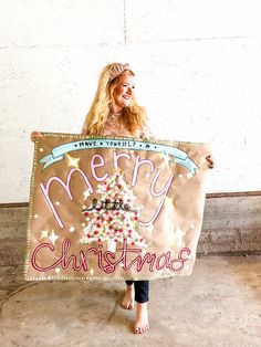 a woman holding up a merry christmas sign with a tree on it's side