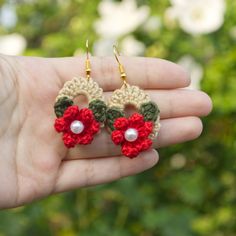 small crocheted flower earrings with pearls in the middle on a person's hand