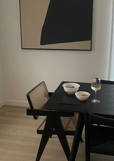 a black table with two bowls of food and a glass of wine on it in front of a painting