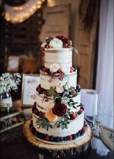 a three tiered wedding cake with flowers and berries on the top is sitting on a table