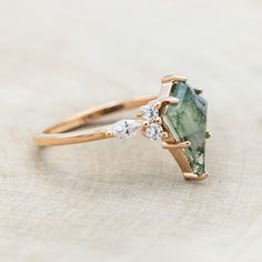 an engagement ring with a green stone and two white diamonds on the side, sitting on a piece of wood