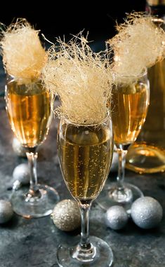 three glasses filled with champagne sitting on top of a table next to silver balls and tinsel