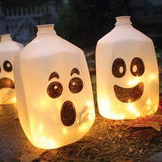 three lighted bottles with faces on them sitting in the grass and one has eyes drawn on it