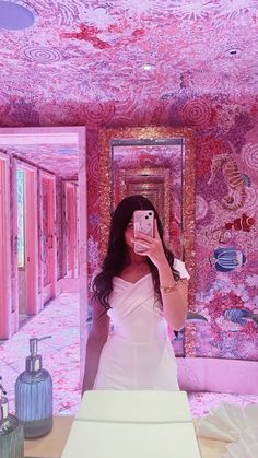 a woman taking a selfie in front of a mirror with pink walls and ceiling